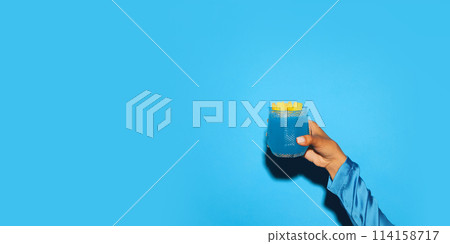 Female hand holding sweet and sour blue tropical cocktail with pineapple slice against bright blue background Female hand holding sweet and sour blue tropical cocktail with pineapple slice against bright blue background 114158717