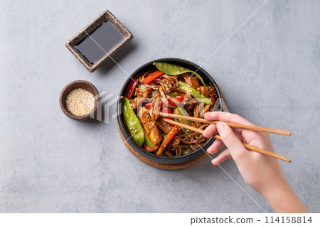 Stir-fry with soba noodles, meat and vegetables in black plate on a light background 114158814