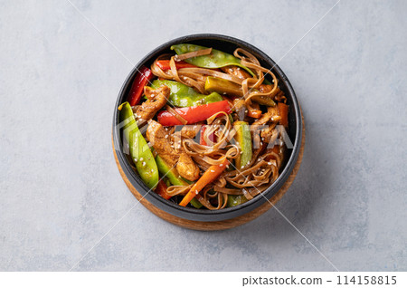 Stir-fry with soba noodles, meat and vegetables in black plate on a light background. 114158815