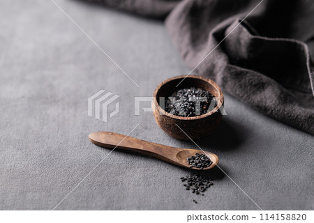 Black sesame seeds in a wooden bowl on a dark background with napkin. Black sesame seeds in a wooden bowl on a dark background with napkin. 114158820