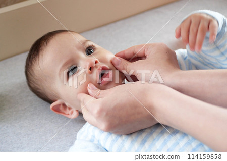 Happy Baby boy lying, mother's hand pressing her cheeks 114159858