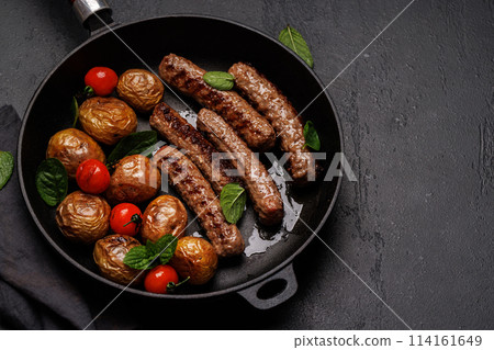 Delicious grilled sausages and potatoes in a sizzling frying pan 114161649