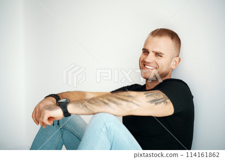 Smiling handsome man sitting on floor looking to camera with copy space Smiling handsome man sitting on floor looking to camera with copy space 114161862