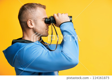 Young man looking through binoculars isolated over yellow background 114161873
