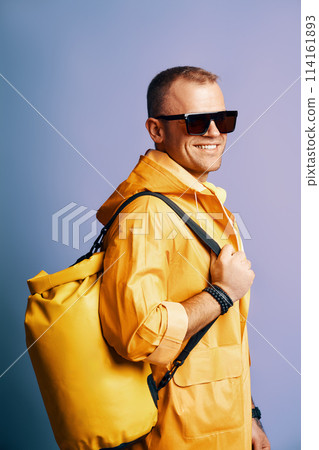 Trendy smiling man in yellow raincoat and sunglasses over blue background. 114161893