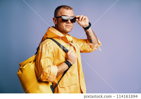 Trendy young man in yellow raincoat and sunglasses over blue background. Trendy young man in yellow raincoat and sunglasses over blue background. 114161894