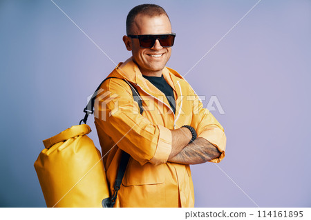 Trendy smiling man in yellow raincoat and sunglasses over blue background. Trendy smiling man in yellow raincoat and sunglasses over blue background. 114161895