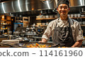 A chef is smiling and standing in a kitchen with a tray of food in front of him. The kitchen is well-equipped with various utensils and appliances, including a sink, a refrigerator, and a microwave 114161960