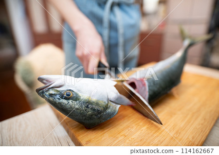 Woman cutting off the head of a fish 114162667