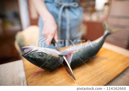 Woman cutting off the head of a fish Woman cutting off the head of a fish 114162668