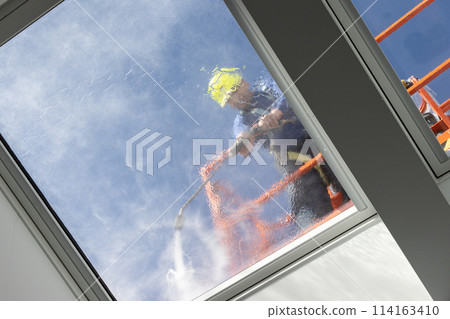 Worker on a cherry picker cleaning a roof windows with high pressure water jet. Low angle shot 114163410