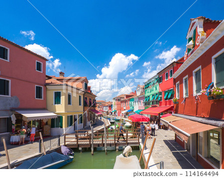 A bridge over a waterway in a city surrounded by colorful buildings (Burano, Italy) 114164494