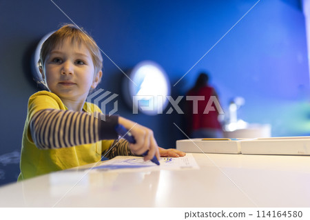 A young boy is sitting at a table with a blue marker in his hand 114164580