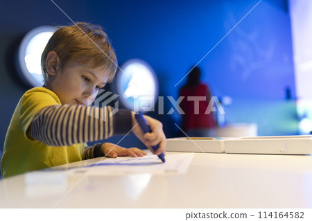 A boy is drawing on a piece of paper with a blue marker A boy is drawing on a piece of paper with a blue marker 114164582