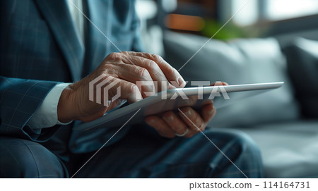 A man in a suit is using a tablet while sitting on a couch A man in a suit is using a tablet while sitting on a couch 114164731