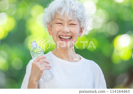 Senior woman drinking water in a park with fresh green leaves Senior woman drinking water in a park with fresh green leaves 114164865