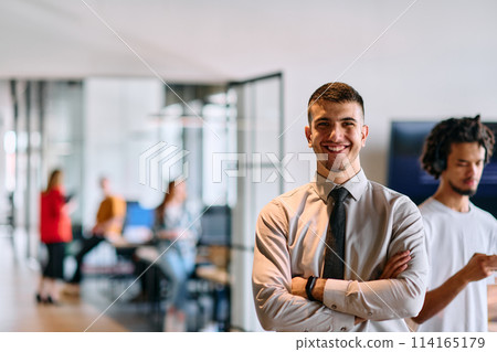 A young business leader stands with crossed arms in a modern office hallway, radiating confidence and a sense of purpose, embodying a dynamic and inspirational presence A young business leader stands with crossed arms in a modern office hallway, radiating confidence and a sense of purpose, embodying a dynamic and inspirational presence 114165179
