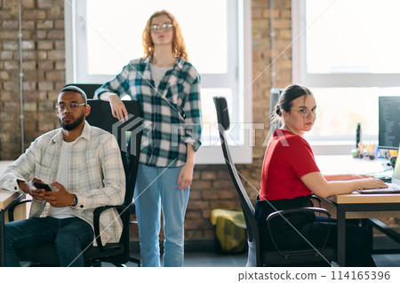 A diverse group of young business individuals congregates in a modern startup coworking center, embodying collaborative innovation and a dynamic atmosphere. 114165396