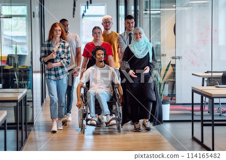A diverse group of young business people congregates within a modern startup's glass-enclosed office, featuring inclusivity with a person in a wheelchair, an African American young man, and a hijab A diverse group of young business people congregates within a modern startup's glass-enclosed office, featuring inclusivity with a person in a wheelchair, an African American young man, and a hijab 114165482