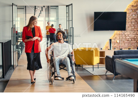 A business leader with her colleague, an African-American businessman who is a disabled person, pass by their colleagues who work in modern offices 114165490