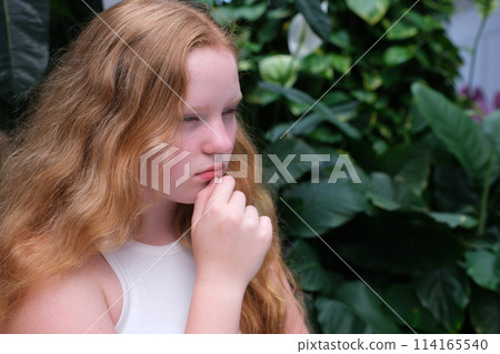 The girl, red-haired, put her hand to her chin, thinking, thinking, dreaming. High quality photo 114165540