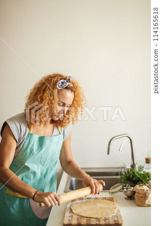 Beautiful young mom and her cute little daughter rolling out dough at home. 114165618