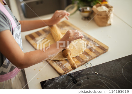 Beautiful young mom and her cute little daughter rolling out dough at home. 114165619