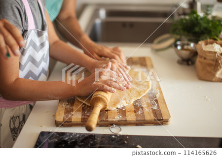 Beautiful young mom and her cute little daughter rolling out dough at home. Beautiful young mom and her cute little daughter rolling out dough at home. 114165626