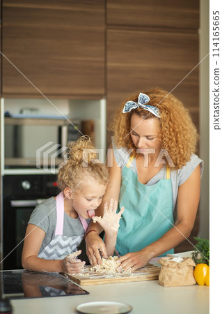 Woman and cute daughter cooking on kitchen, making dough for birthday party. Woman and cute daughter cooking on kitchen, making dough for birthday party. 114165665