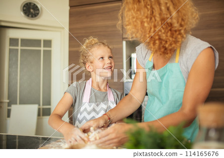 Woman and cute daughter cooking on kitchen, making dough for birthday party. 114165676