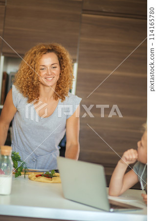 Little girl and her daughter baking cookies at home, reading recipe on laptop. 114165780