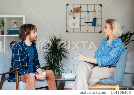 Depressed male patient having psychotherapy session with counselor at mental health clinic. Man with emotional problems consulting professional therapist i comfy office. Psychological help service. 114166300