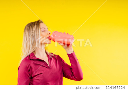 Happy beautiful brunette woman with water bottle or proteine shake on yellow background 114167224