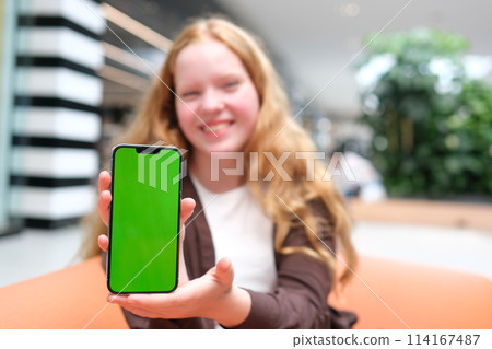 young cheerful girl against backdrop of the lake points to phone screen of smartphone. finger smiles laughs Good advertising for walks travel fun girl with fair skin in black clothes beautiful teeth young cheerful girl against backdrop of the lake points to phone screen of smartphone. finger smiles laughs Good advertising for walks travel fun girl with fair skin in black clothes beautiful teeth 114167487