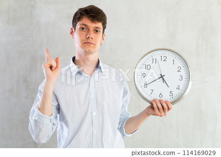 Young guy posing with clock in studio Young guy posing with clock in studio 114169029