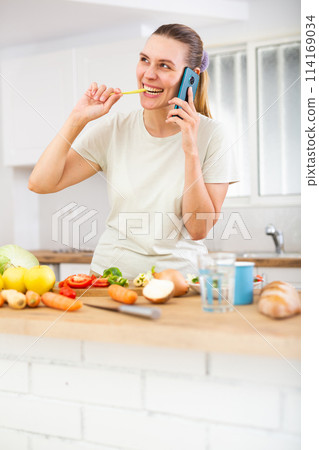 Emotional young woman standing in home kitchen and chatting on phone 114169034