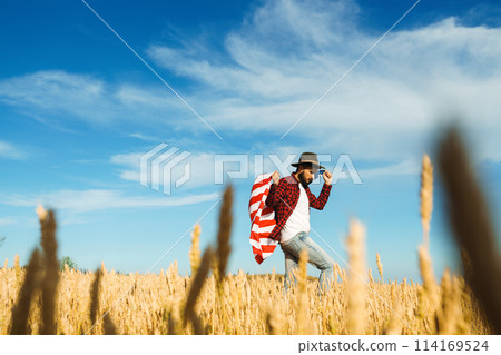 4th of July. American Flag. Traveler with the flag of America. The man in a hat, a backpack, a shirt and jeans. 4th of July. American Flag. Traveler with the flag of America. The man in a hat, a backpack, a shirt and jeans. 114169524