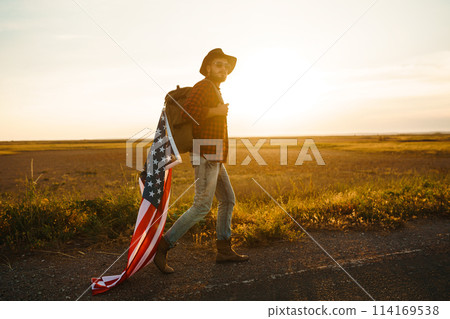 4th of July. American Flag. Traveler with the flag of America. The man in a hat, a backpack, a shirt and jeans. 4th of July. American Flag. Traveler with the flag of America. The man in a hat, a backpack, a shirt and jeans. 114169538