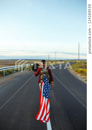 4th of July. American Flag. Traveler with the flag of America. The man in a hat, a backpack, a shirt and jeans. 114169539