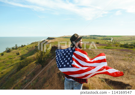 4th of July. American Flag. Traveler with the flag of America. The man in a hat, a backpack, a shirt and jeans. 4th of July. American Flag. Traveler with the flag of America. The man in a hat, a backpack, a shirt and jeans. 114169547