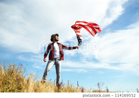 4th of July. American Flag. Traveler with the flag of America. The man in a hat, a backpack, a shirt and jeans. 4th of July. American Flag. Traveler with the flag of America. The man in a hat, a backpack, a shirt and jeans. 114169552