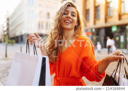 Stylish woman with shopping bag walking at sunny street in bright dress. Concept of sales, discounts Stylish woman with shopping bag walking at sunny street in bright dress. Concept of sales, discounts 114169844