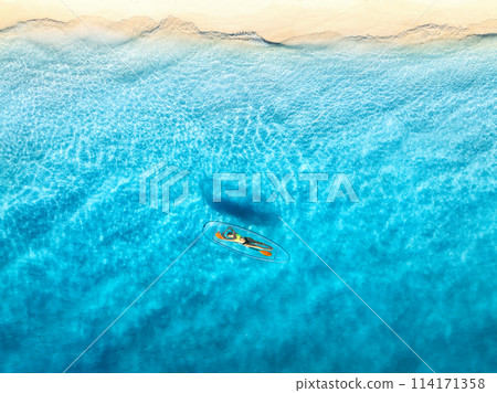 Aerial view of young woman lying on transparent canoe in blue se Aerial view of young woman lying on transparent canoe in blue se 114171358