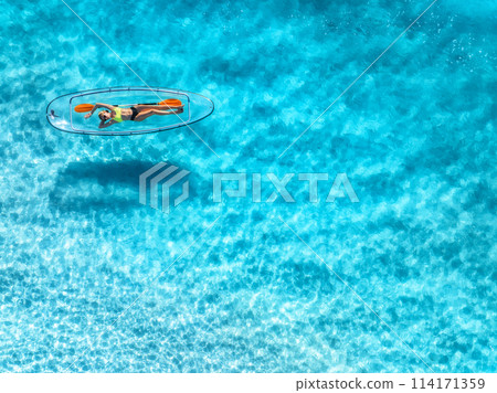 Aerial view of young woman lying on transparent canoe in blue se Aerial view of young woman lying on transparent canoe in blue se 114171359