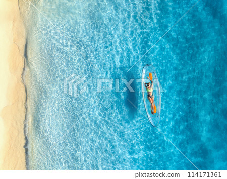 Aerial view of young woman lying on transparent canoe in blue se Aerial view of young woman lying on transparent canoe in blue se 114171361