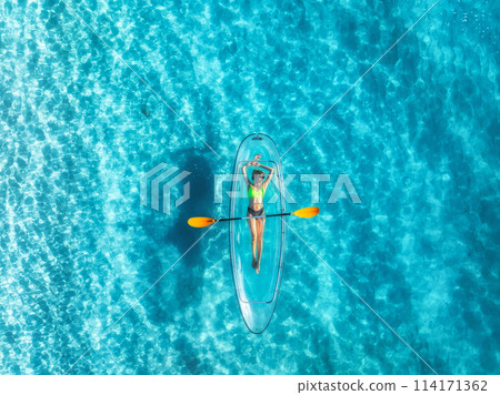 Aerial view of young woman lying on transparent canoe in blue se 114171362