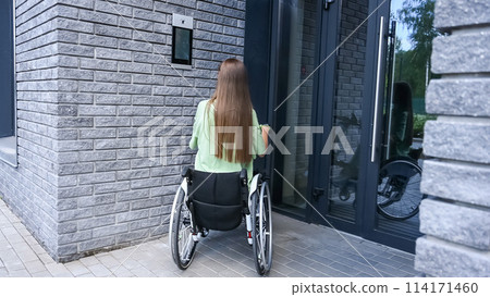 A woman in a wheelchair with an assistive device for manual control enters the entrance. Electric hand bike. A woman in a wheelchair with an assistive device for manual control enters the entrance. Electric hand bike. 114171460