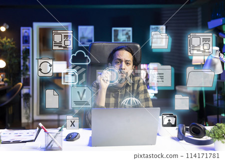 Portrait of man in home office doing business tasks on laptop, online connectivity concept. Freelancer using augmented reality tech to interact with files on notebook system, close up on icons Portrait of man in home office doing business tasks on laptop, online connectivity concept. Freelancer using augmented reality tech to interact with files on notebook system, close up on icons 114171781