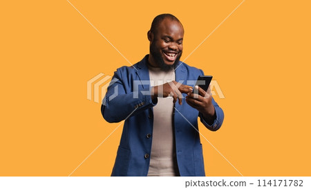 Happy man adding payment method on phone website, delighted to take advantage of promotions, studio background. Person thrilled to do internet shopping, typing credit card data on smartphone, camera B 114171782