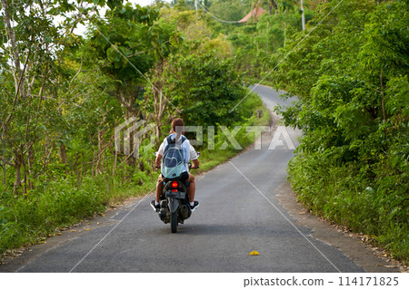 A person on a motorcycle rides a scenic asphalt road in Asia. A person on a motorcycle rides a scenic asphalt road in Asia. 114171825